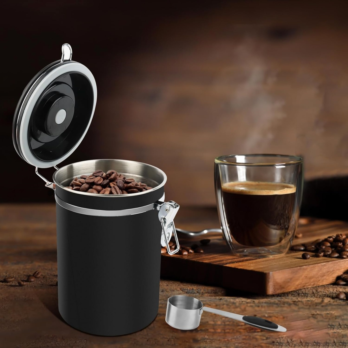 Ein offener schwarzer Kaffeebehälter gefüllt mit Bohnen neben einem Glas Kaffee.
