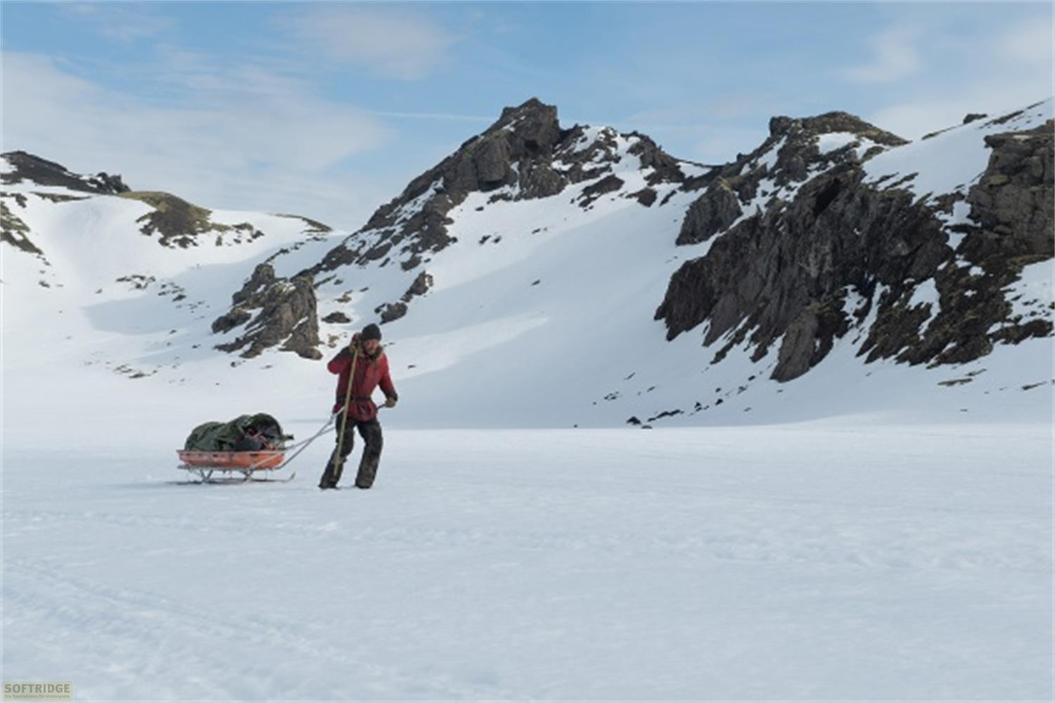 Una persona tira una slitta in un paesaggio innevato con montagne.
