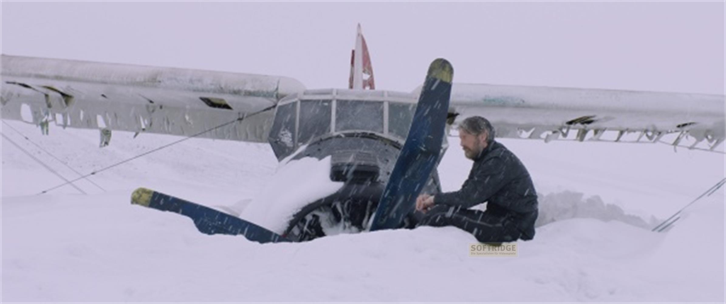 Un uomo seduto nella neve accanto al relitto di un aereo coperto di neve.