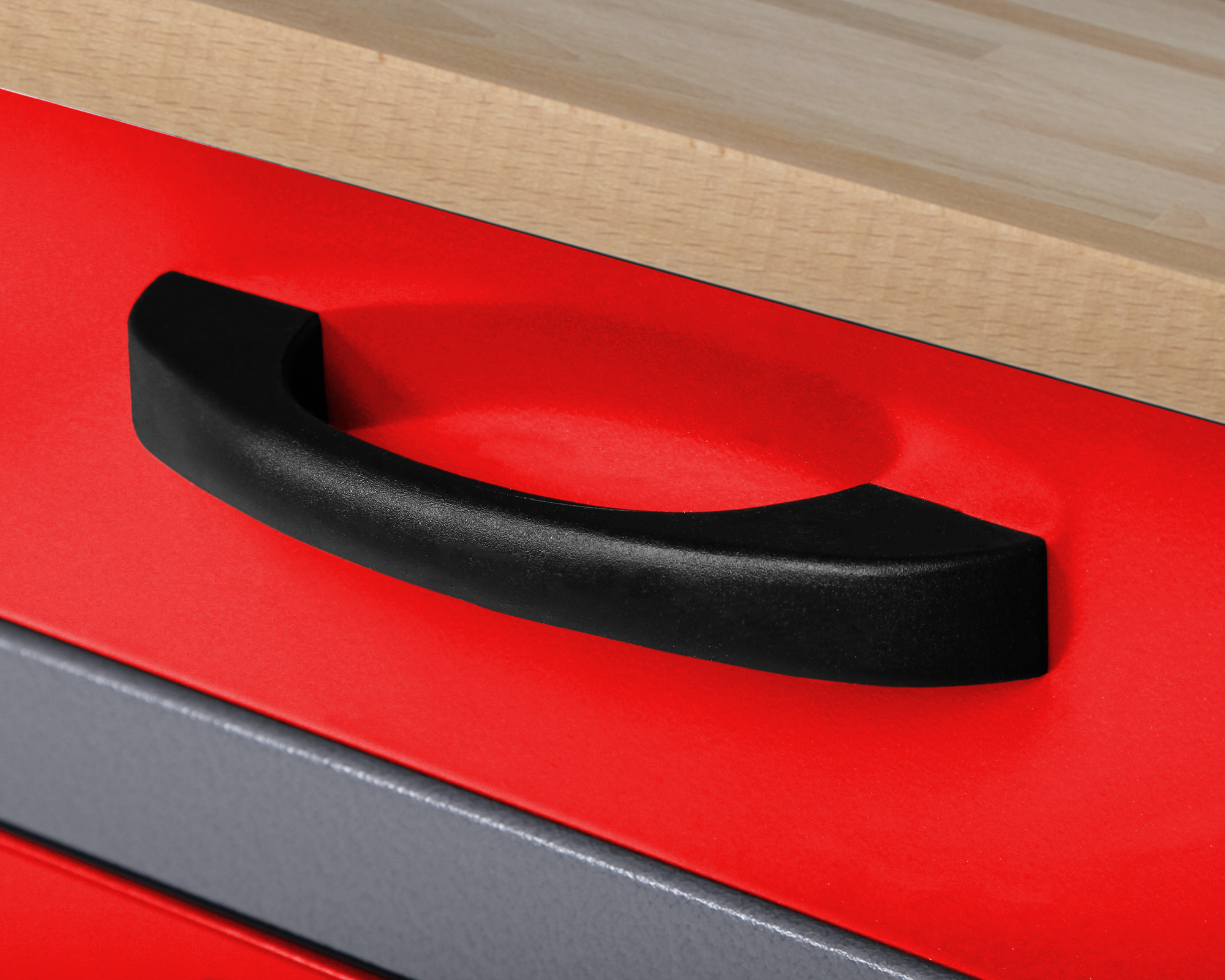 Schwarzer Griff auf roter Schubladenoberfläche mit Holzplatte oben.