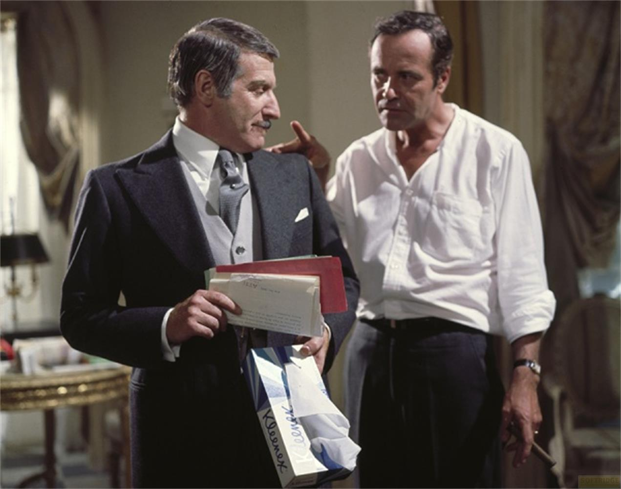Due uomini parlano. Uno indossa un abito, l'altro una camicia bianca.