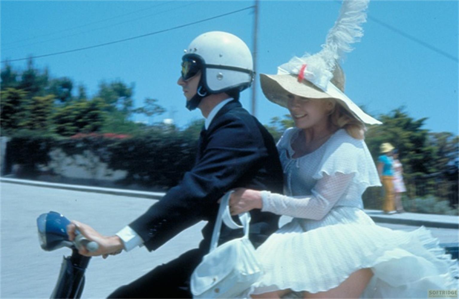 Uomo con casco e donna con cappello guidano uno scooter per strada.