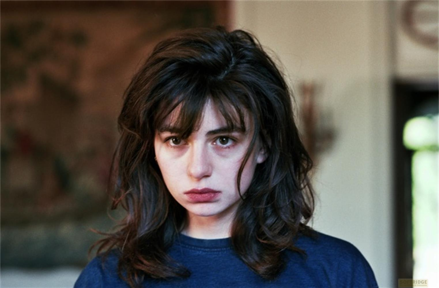 Una giovane donna con capelli scuri e abiti blu guarda pensierosa.
