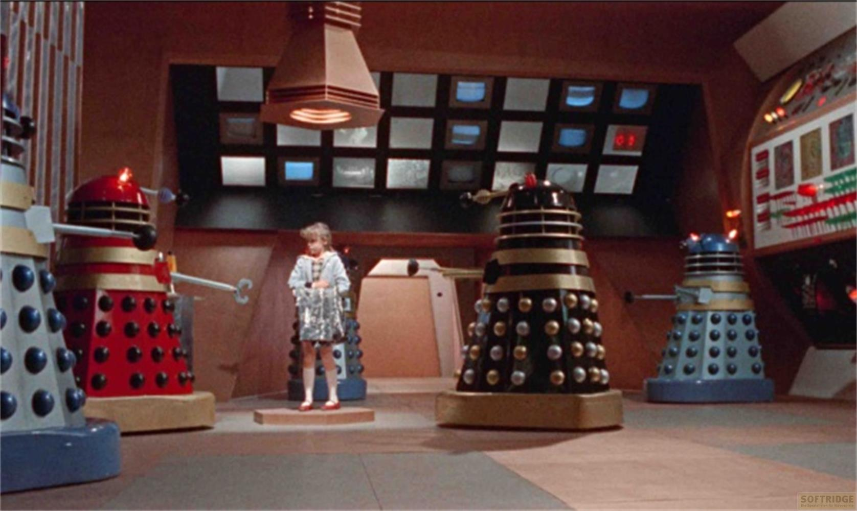 Un bambino è in piedi davanti a diversi Dalek in una stanza con schermi.
