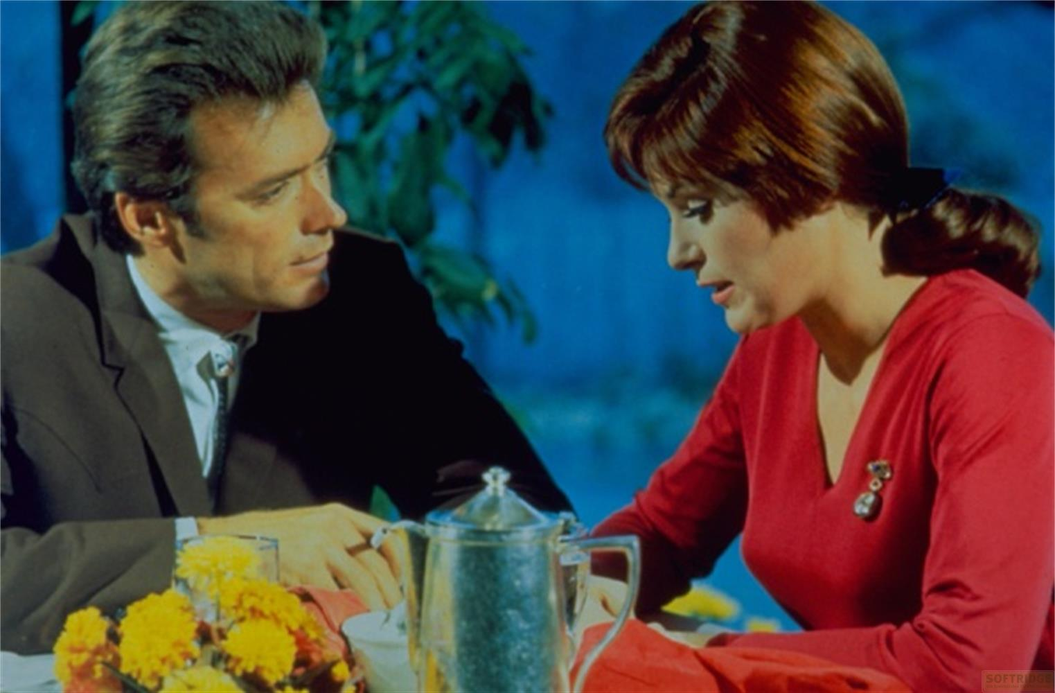 Un homme et une femme assis à une table avec des fleurs et une cafetière.