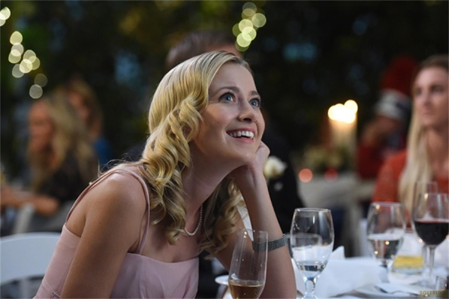 Una donna con riccioli biondi sorride guardando in alto, indossa un vestito rosa.