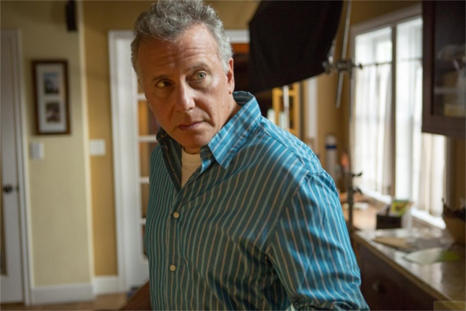 Un homme âgé aux cheveux gris, portant une chemise bleue, regarde à gauche.