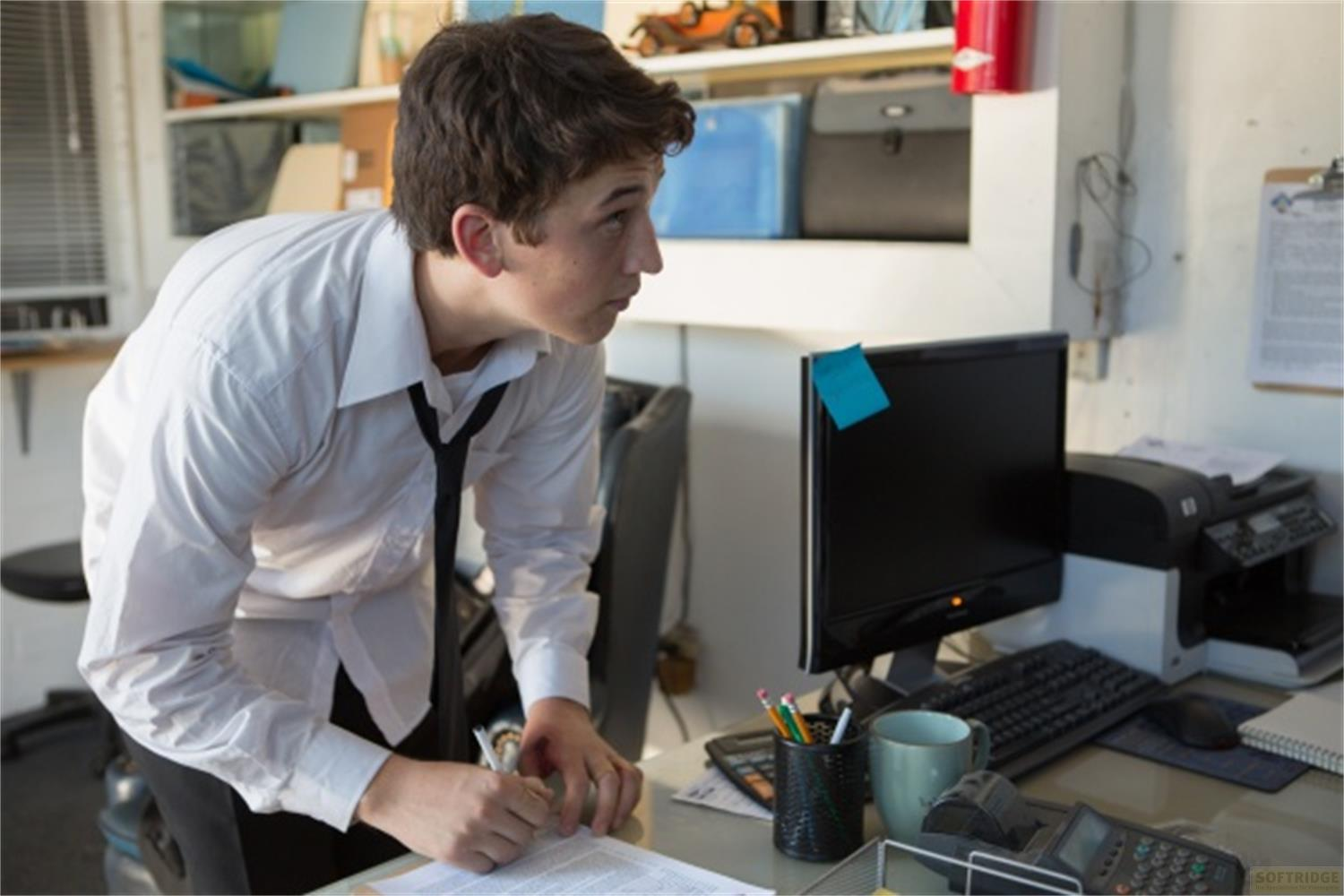 Un garçon en chemise blanche et cravate noire regarde un écran d'ordinateur au bureau.