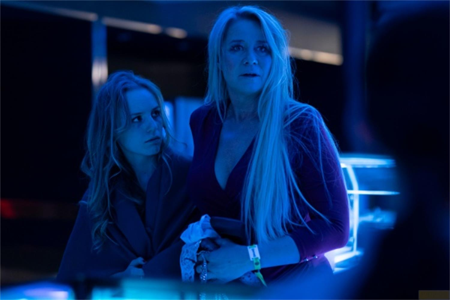 Due donne con i capelli lunghi stanno nella luce blu. Una indossa un vestito viola.