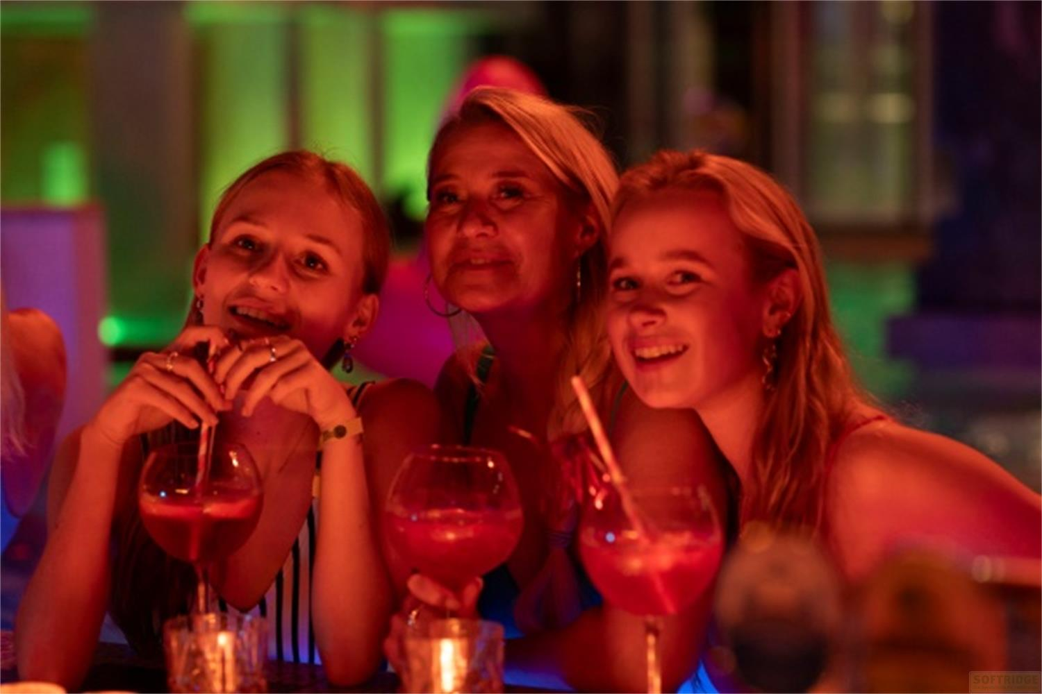Tre donne bevono cocktail con illuminazione colorata.