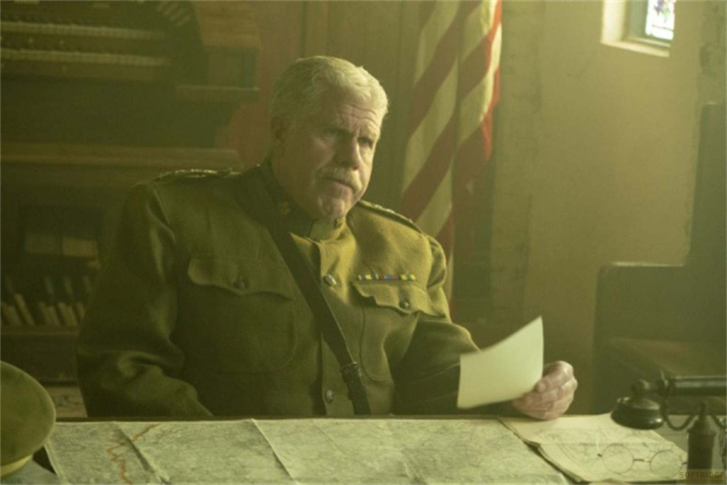 Ufficiale in uniforme militare con baffi legge documento. Bandiera USA sullo sfondo.