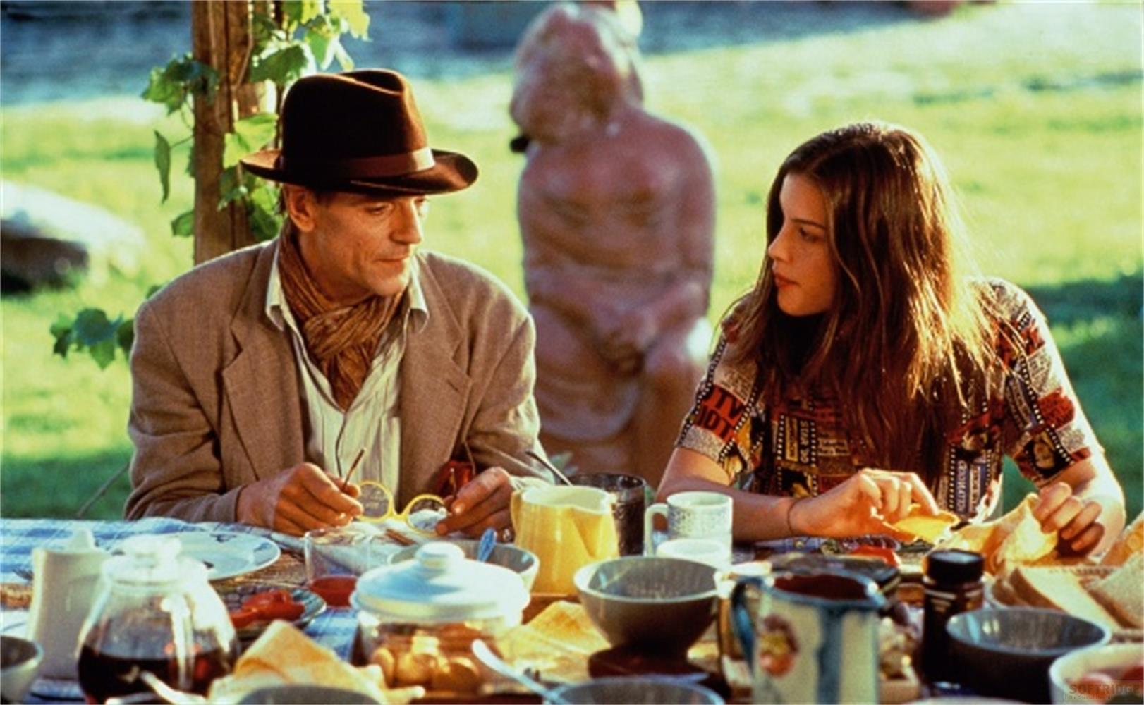 Uomo con cappello e donna a un tavolo esterno con cibo.