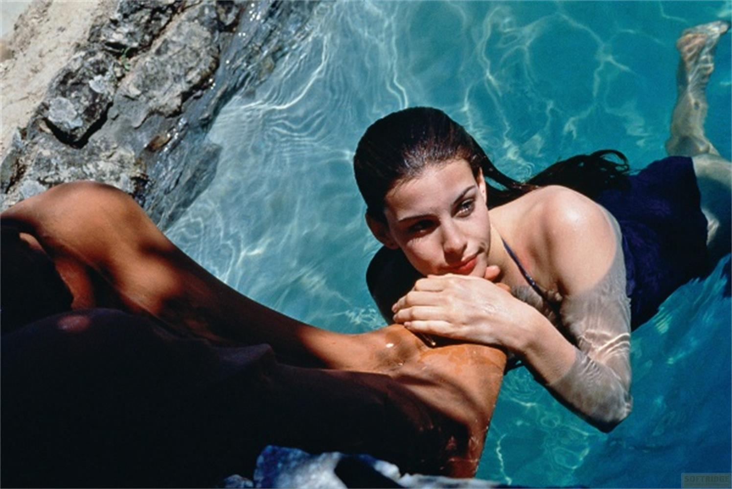 Una donna dai capelli scuri giace nell'acqua blu, guardando verso le rocce.