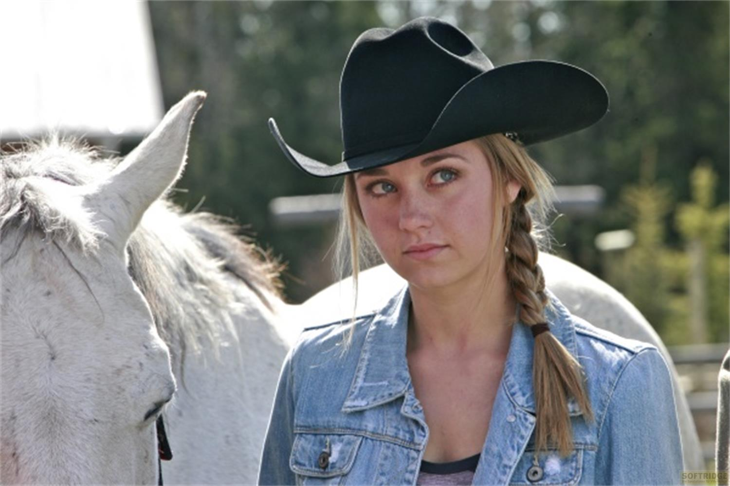 Una giovane donna con cappello da cowboy e giacca di jeans sta accanto a un cavallo bianco.