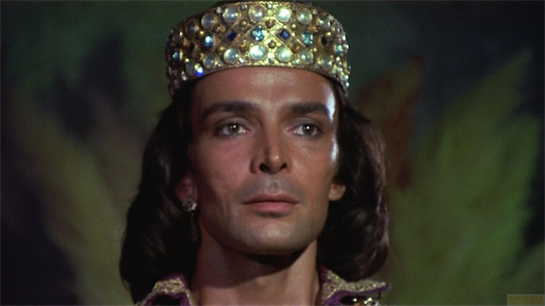 Un uomo con capelli scuri indossa una corona dorata con gioielli.