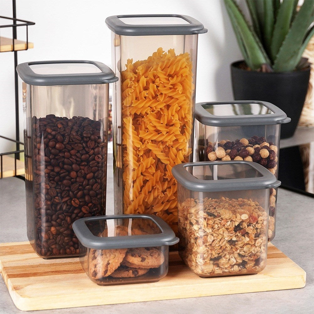 Cinque contenitori ermetici con chicchi di caffè, pasta, cereali, biscotti e noci.
