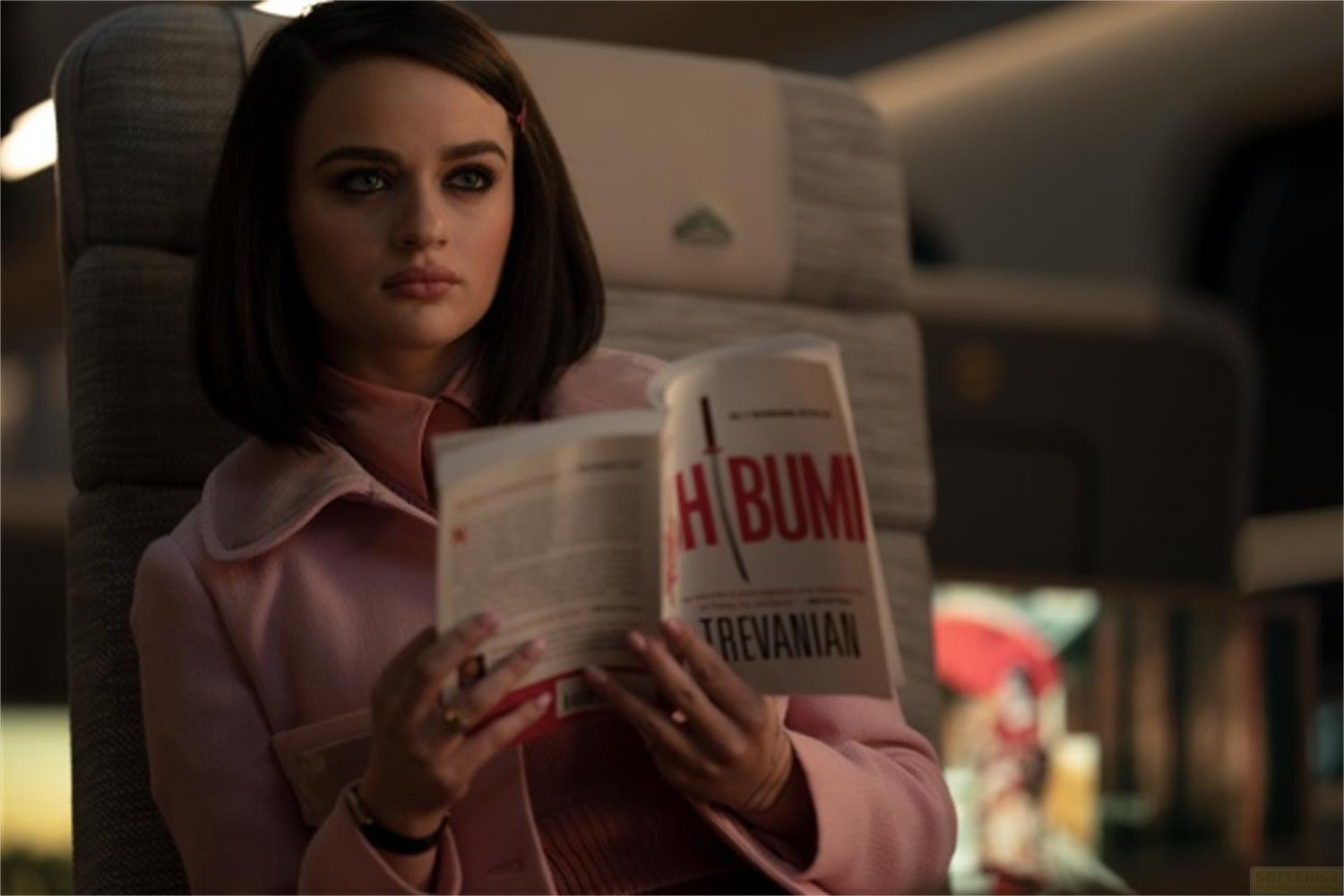 Una donna in cappotto rosa legge un libro su un treno.