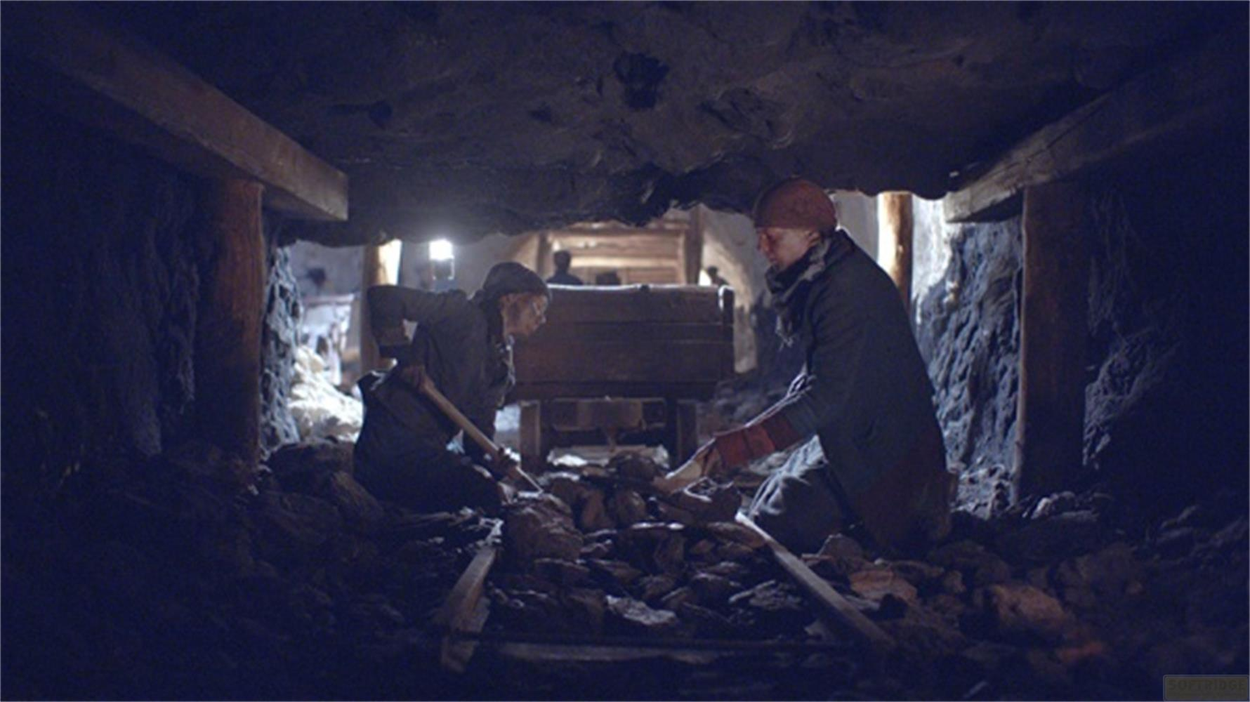Due minatori scavano in un tunnel buio sostenuto da legno, con un carrello da miniera dietro.