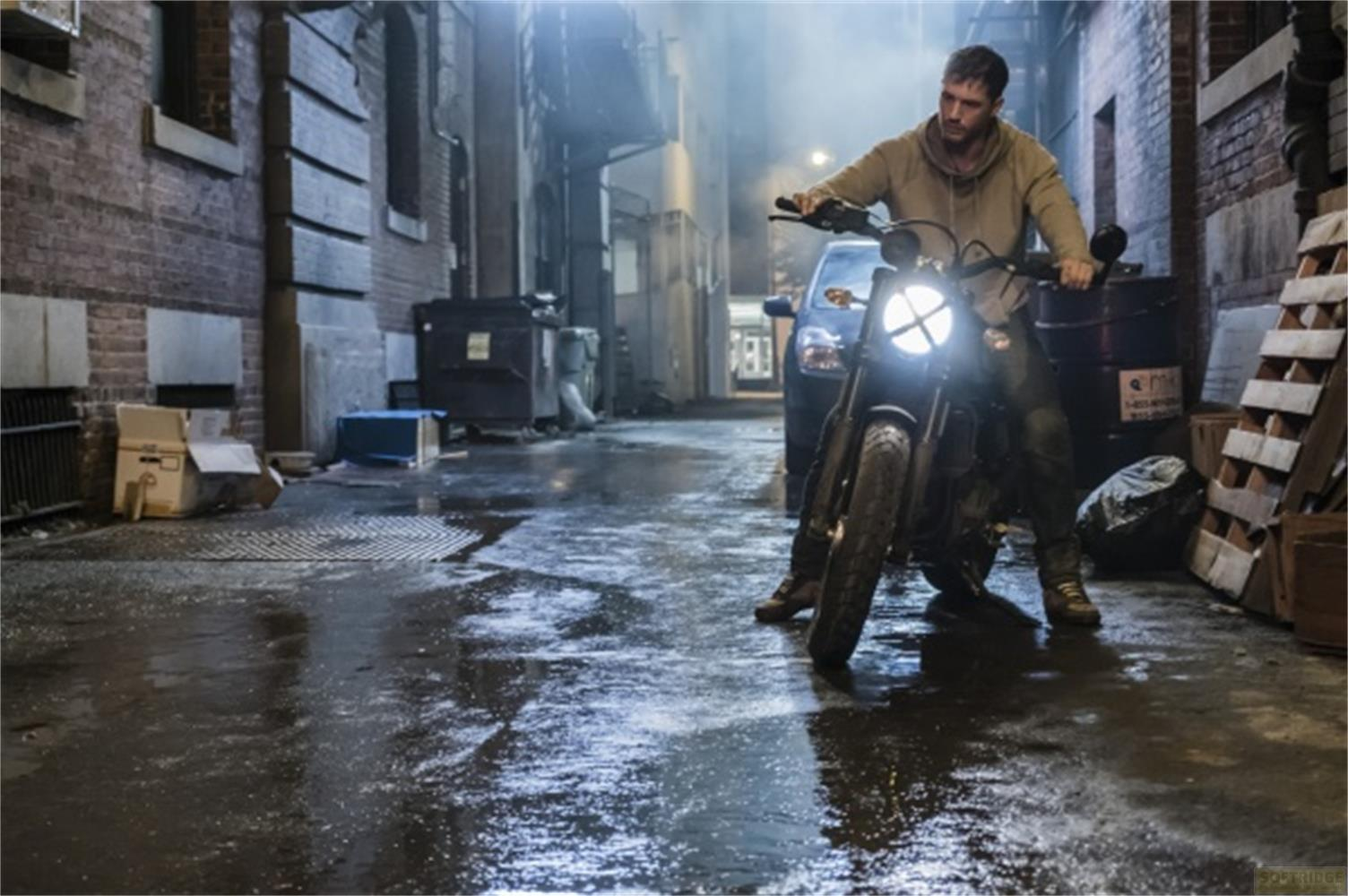 Un uomo su una moto in un vicolo sporco di notte, strada bagnata.