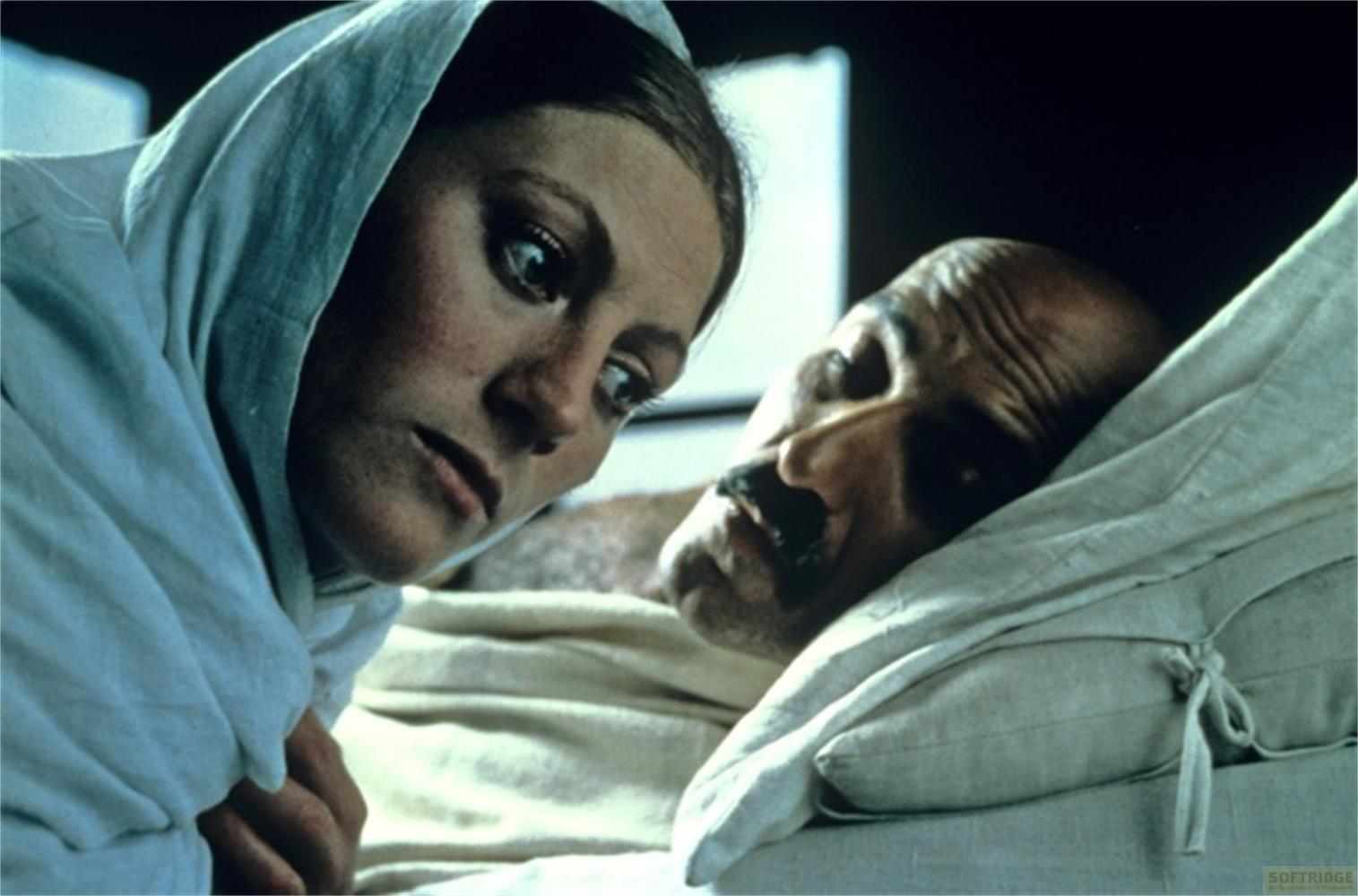 Une femme avec un foulard bleu regarde avec inquiétude un homme allongé dans un lit.