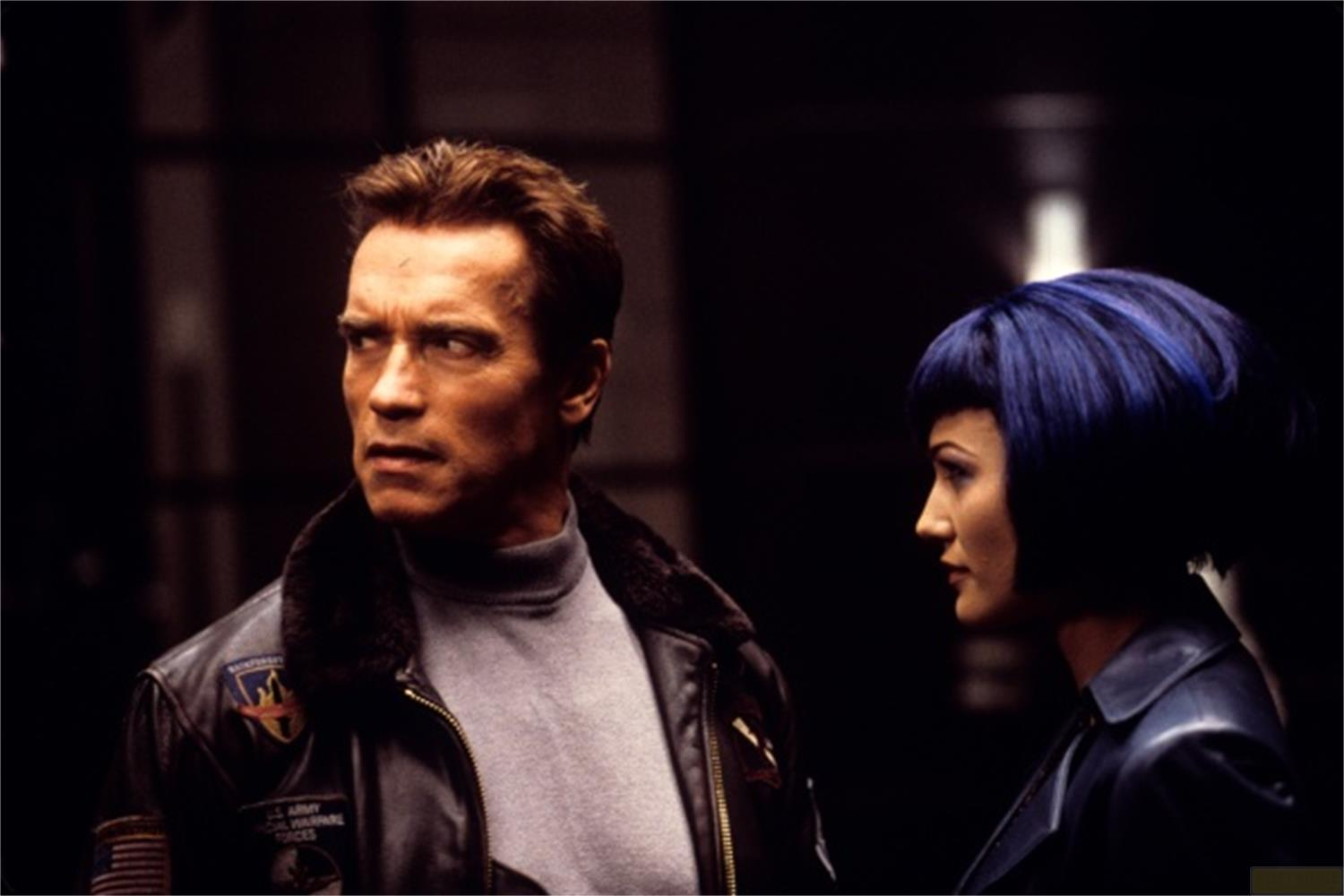 Arnold Schwarzenegger et une femme aux cheveux bleus regardent à gauche.