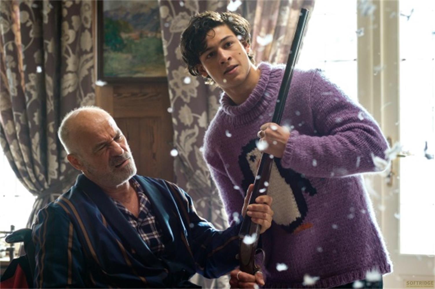 Un uomo in un maglione viola con pinguino tiene un fucile sopra un uomo anziano.