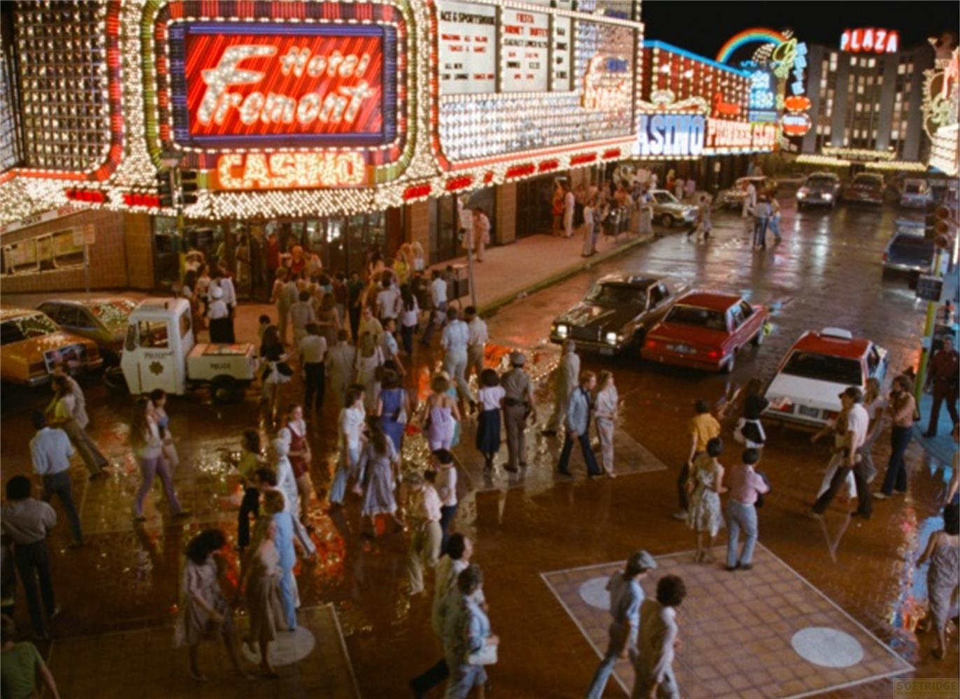 Strada Fremont bagnata di notte con insegne al neon, auto e molte persone.