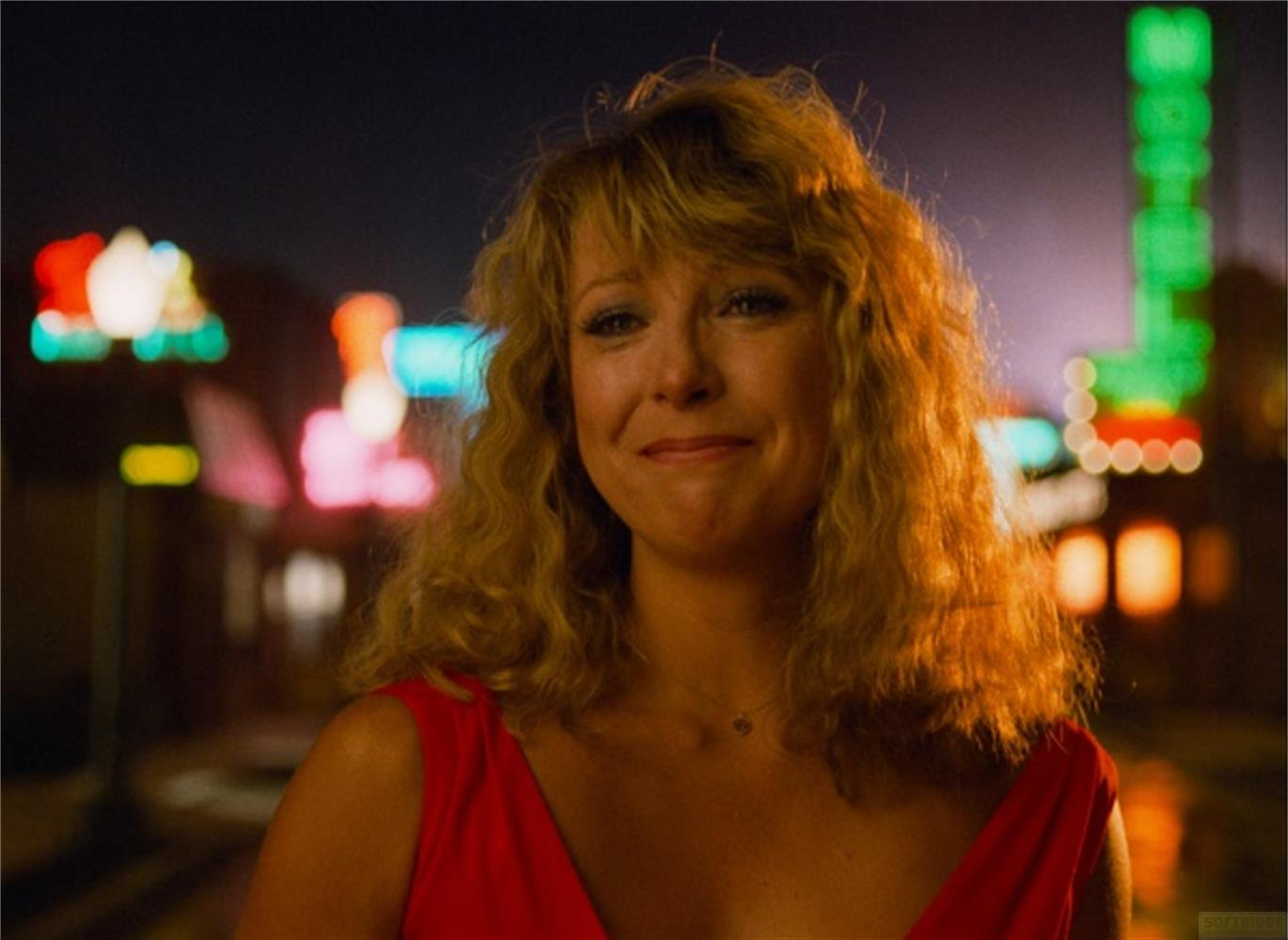 Donna con ricci biondi in abito rosso ride davanti alle luci.