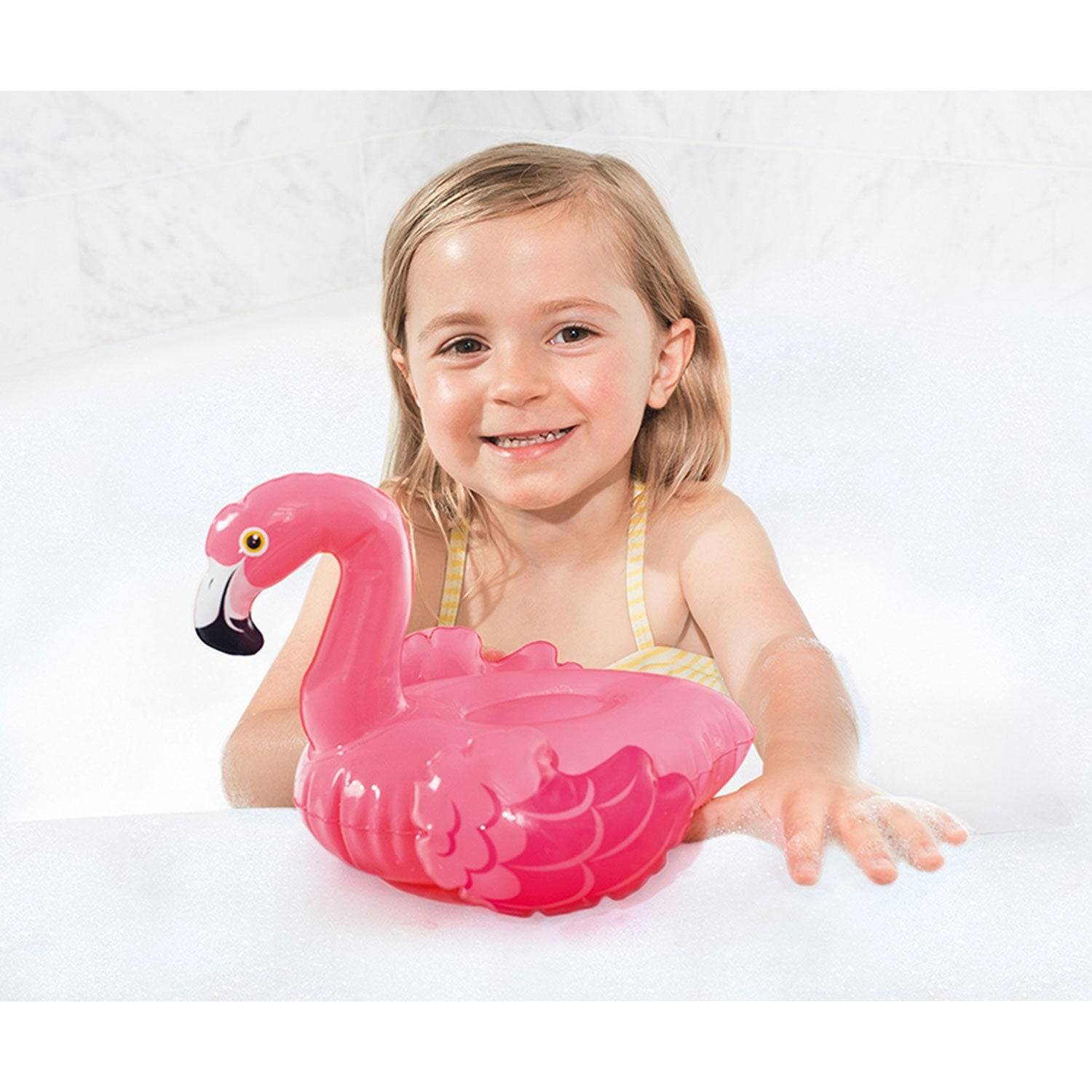 Una niña pequeña sostiene un flamenco inflable rosa en una bañera con espuma.