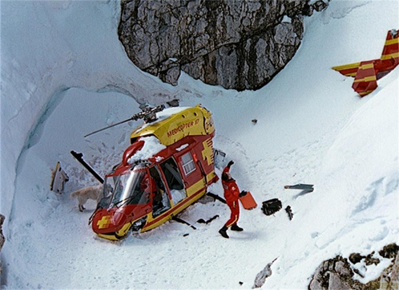 Un elicottero rosso e giallo nella neve, una persona in rosso vicino.