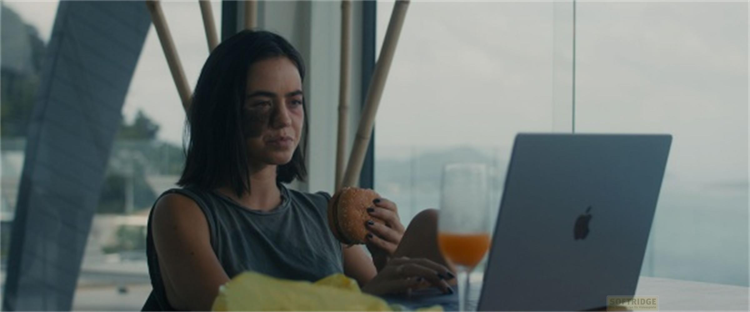 Donna con livido sul viso mangia hamburger davanti a laptop e succo d'arancia.