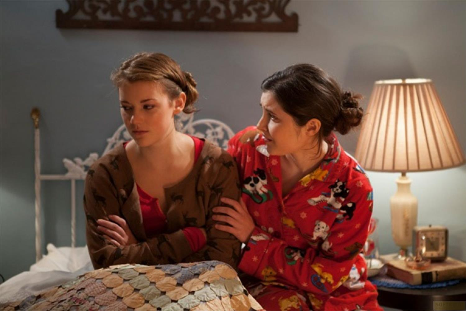 Due giovani donne in pigiama sedute su un letto. Una conforta l'altra.