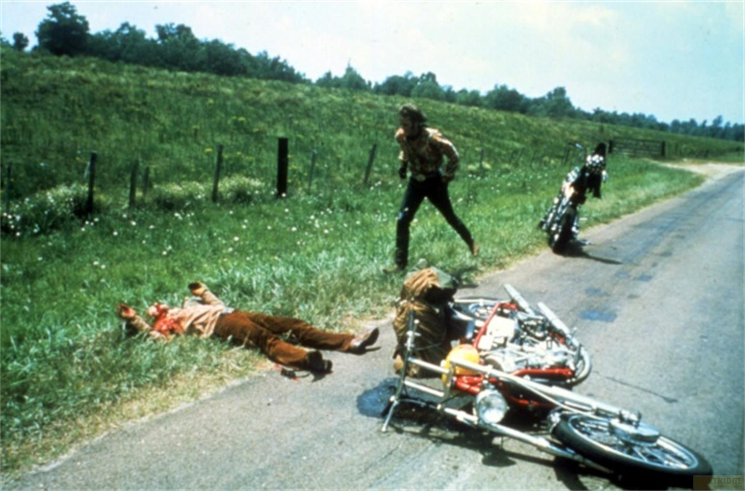 Un homme gît au sol près d'une moto renversée ; un autre homme court.