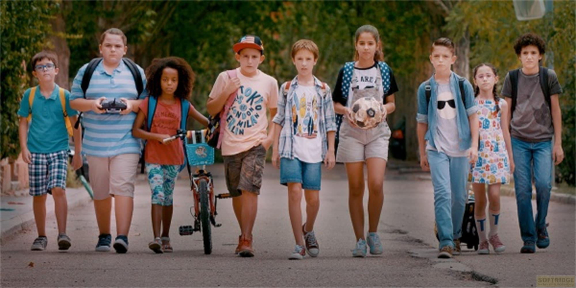 Bambini che camminano per strada, alcuni con zaini, uno con un pallone.