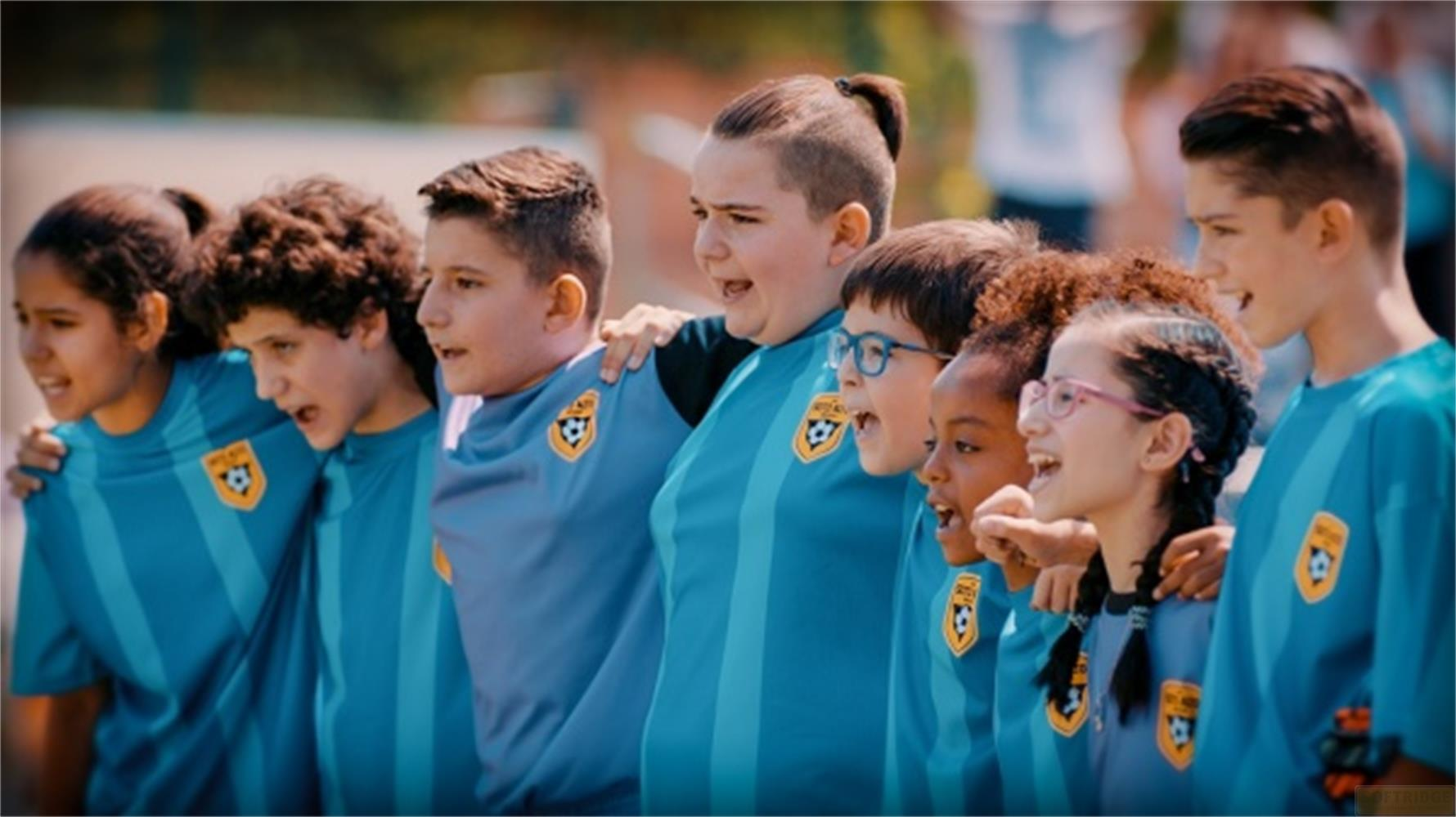 Un gruppo di bambini in maglie da calcio blu sta insieme a fare il tifo.