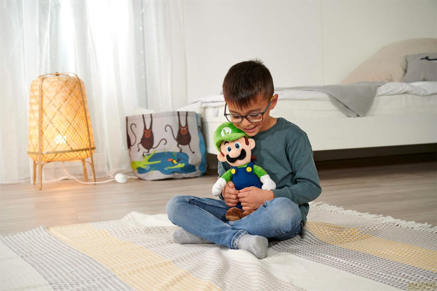 Ein Junge sitzt auf einem Teppich und hält eine Luigi-Puppe. Im Hintergrund ein Nachttisch und eine Lampe.