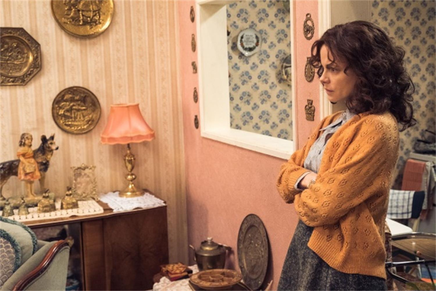 Una donna con un cardigan di lana arancione sta con le braccia incrociate.