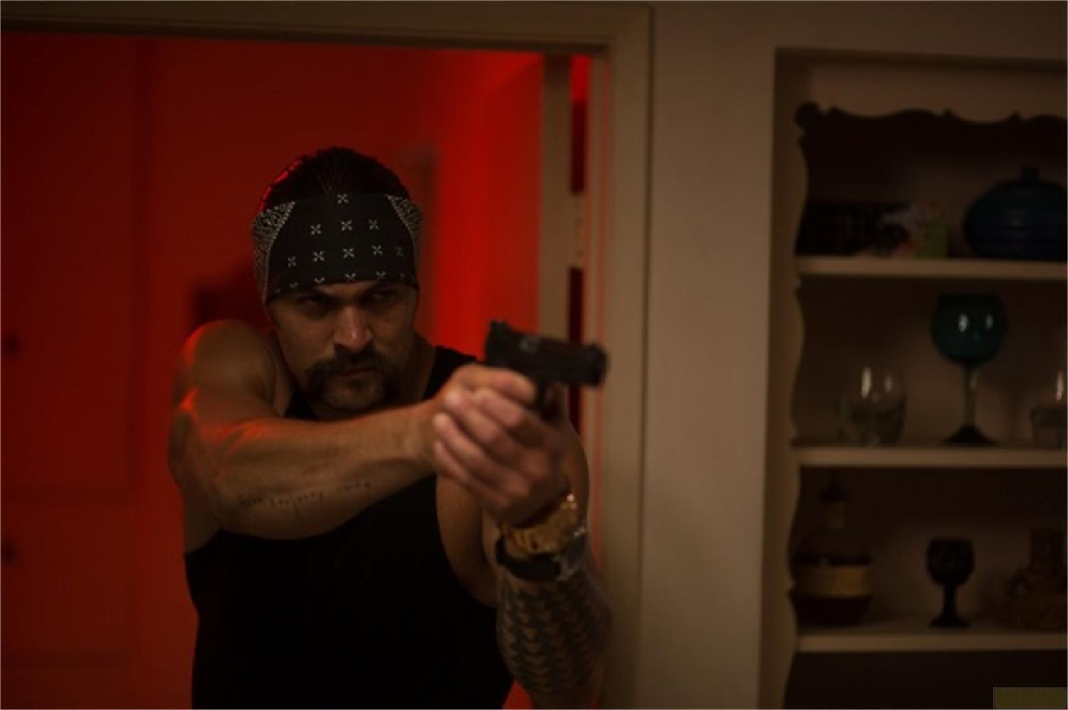 Un uomo con bandana e canottiera nera tiene una pistola.