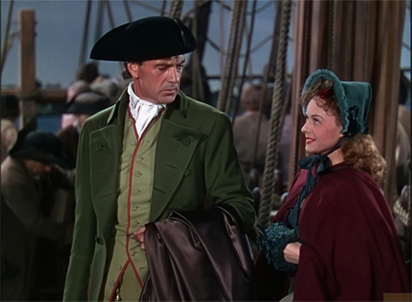 Un uomo in verde e una donna in rosso si trovano sul ponte di una nave.
