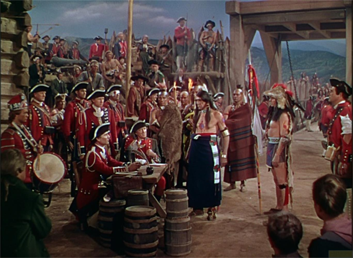 Nativi americani in abiti tradizionali interagiscono con soldati in uniforme rossa.
