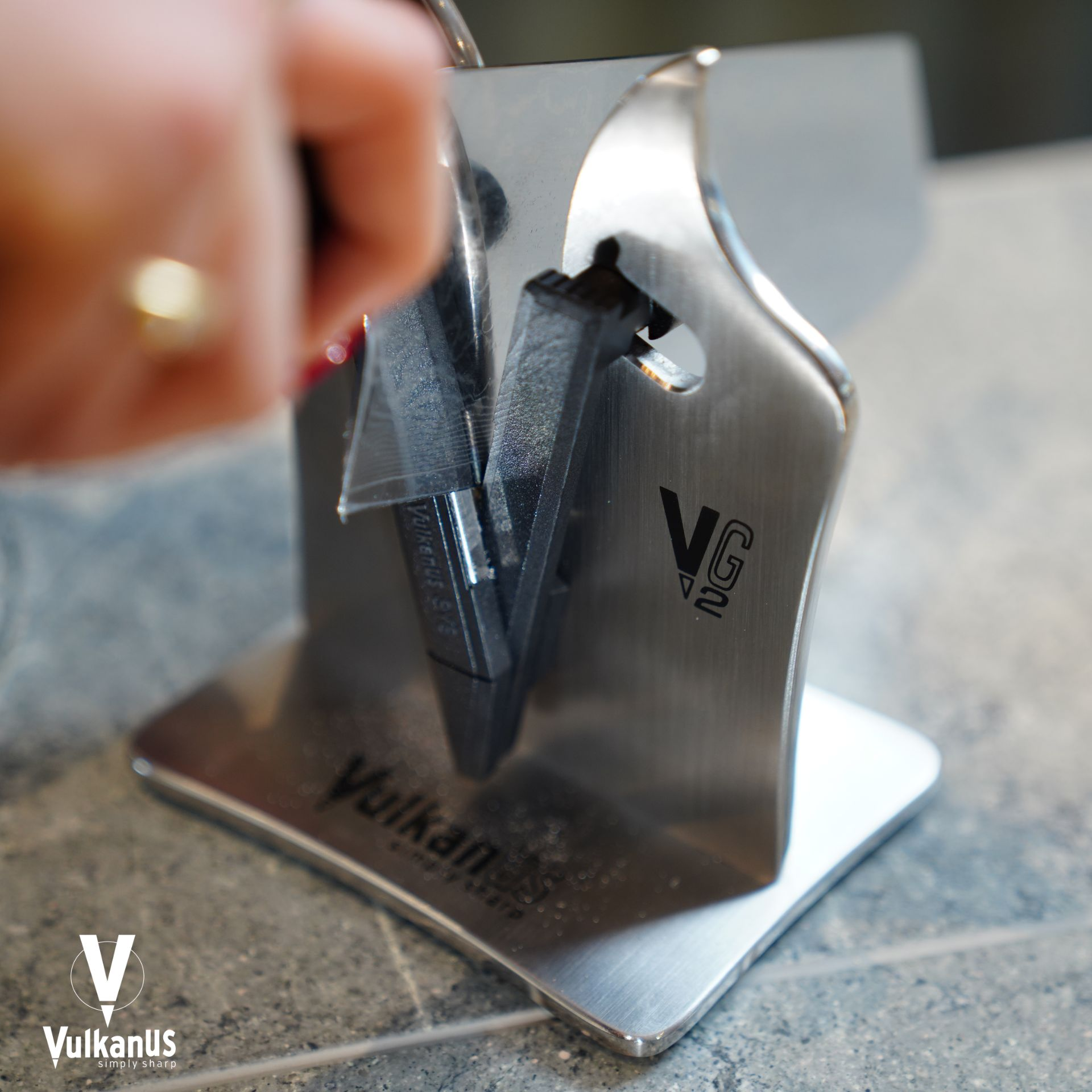 Une main avec une bague ajuste un aiguiseur métallique noir avec logo VG2.