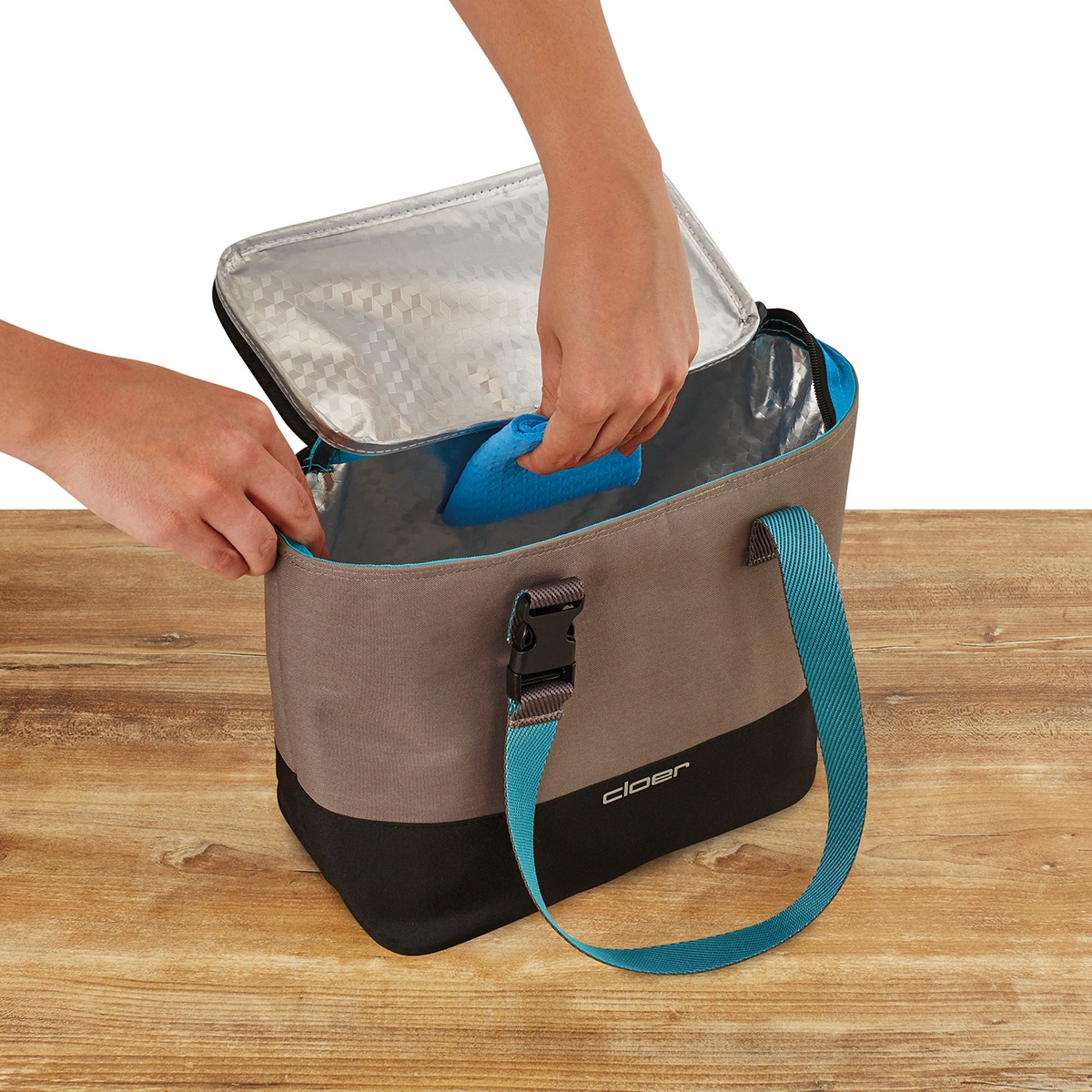 Hände legen einen blauen Kühlakku in eine graue Kühltasche.