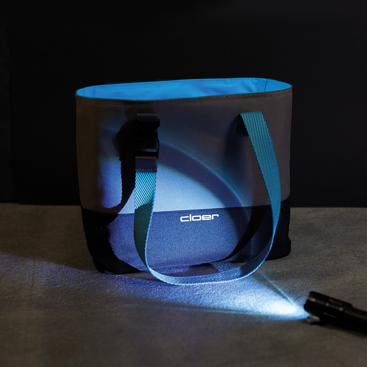 Graue Tasche mit blauen Trägern, beleuchtet von einer Taschenlampe.