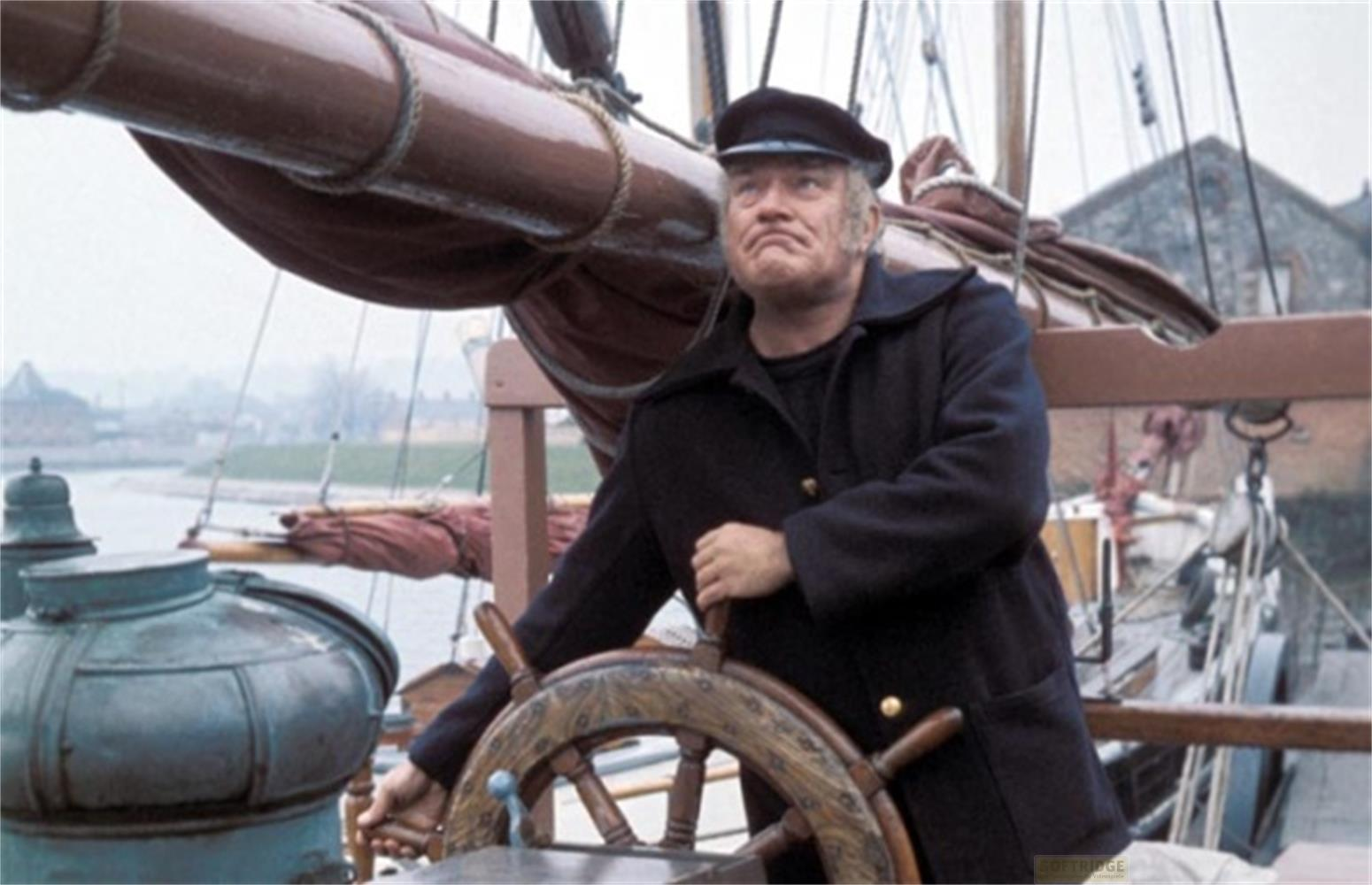 Un uomo in abiti scuri e berretto guida una nave in banchina.
