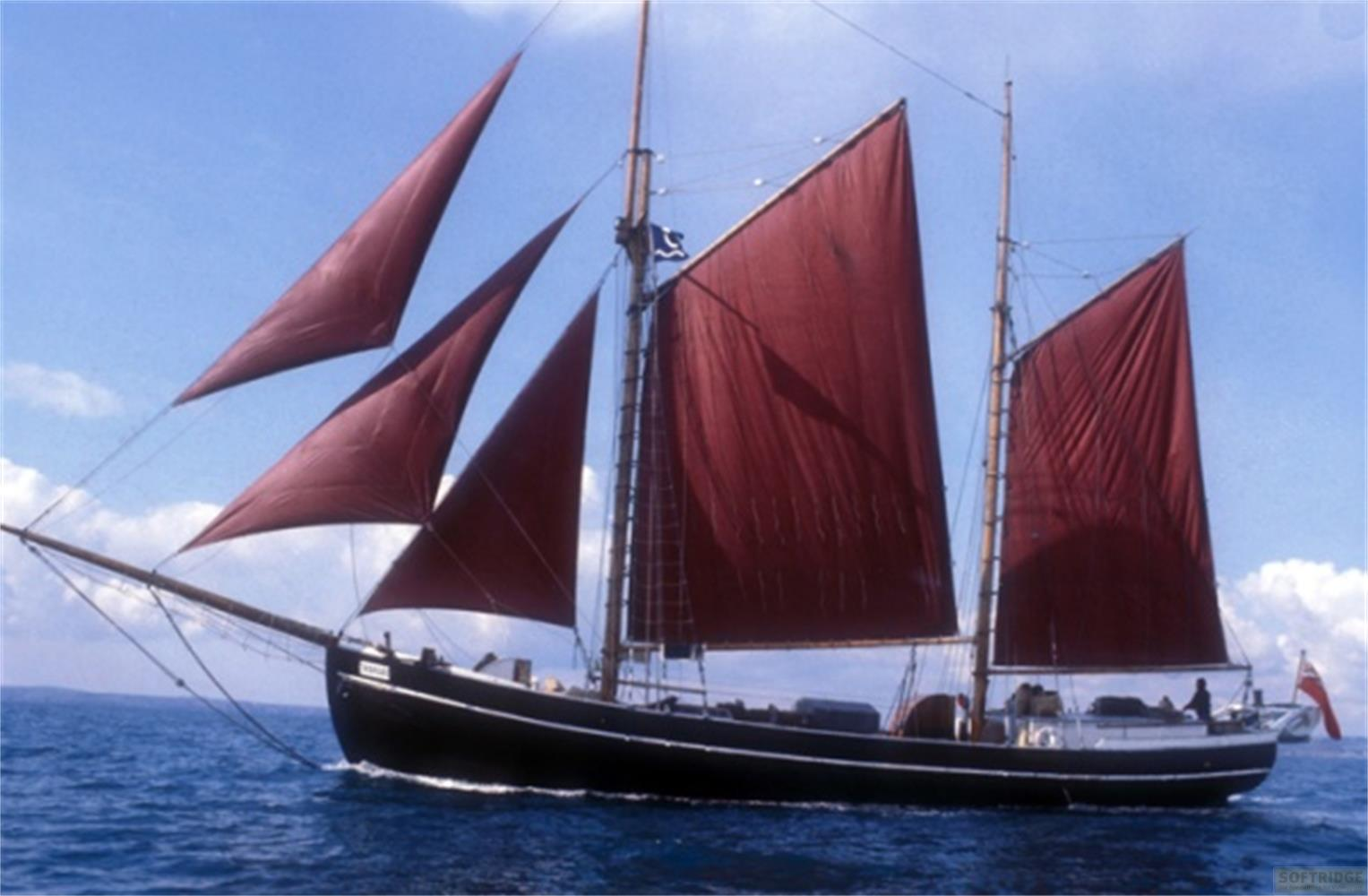 Una barca a vela con vele rosse naviga sul mare blu.