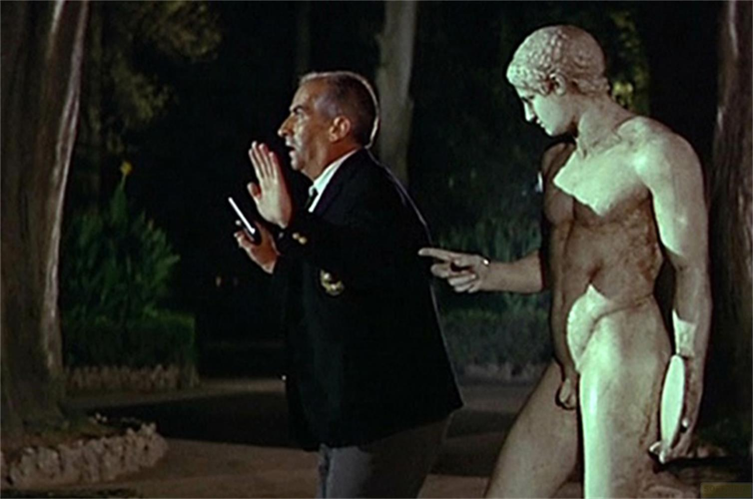 Un uomo in giacca scura indica una statua di uomo nudo.