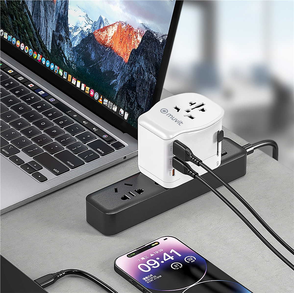 Un portátil, regleta, adaptador de viaje y smartphone sobre un escritorio.