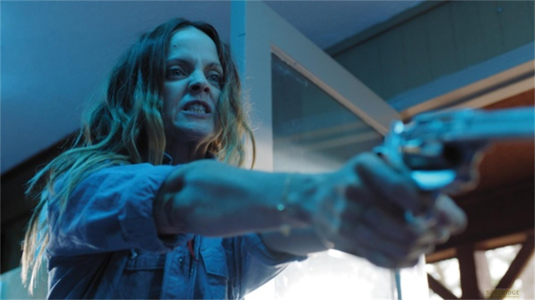 Una donna con i capelli lunghi punta una pistola in una stanza blu.