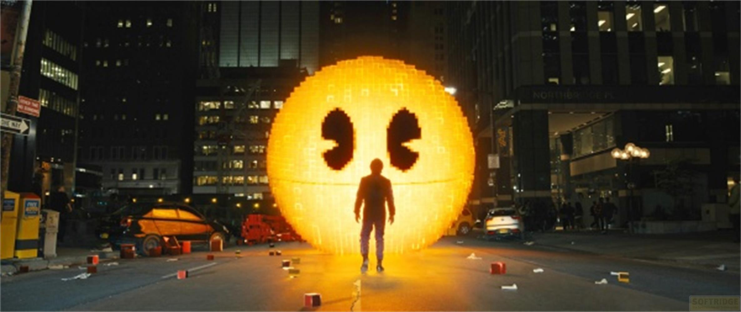 Ein Mann steht vor einer riesigen, leuchtenden Pac-Man-Figur in einer Stadt bei Nacht.