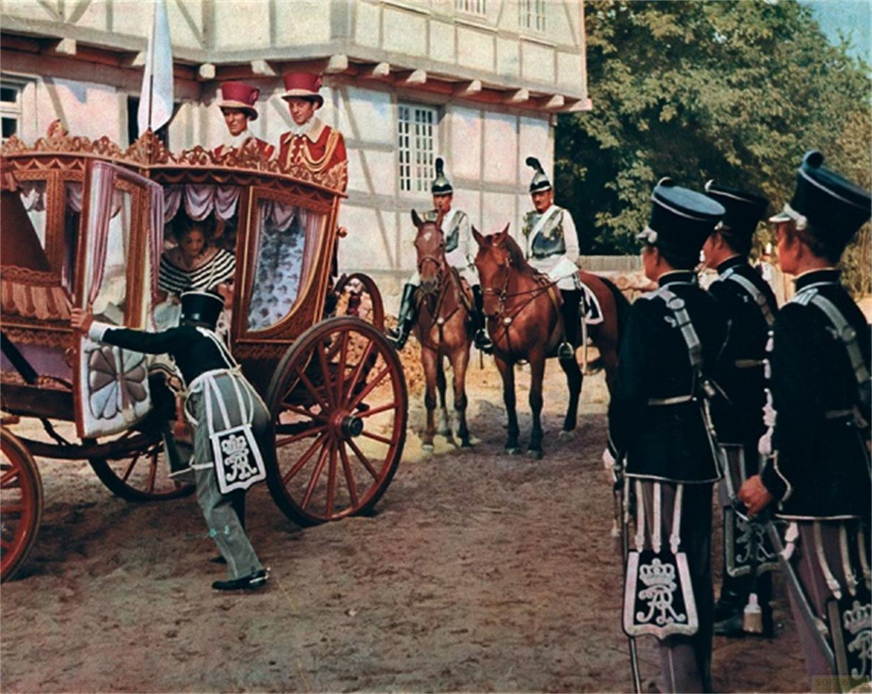 Una carrozza viene spinta da soldati in uniforme con cavalli e un edificio sullo sfondo.